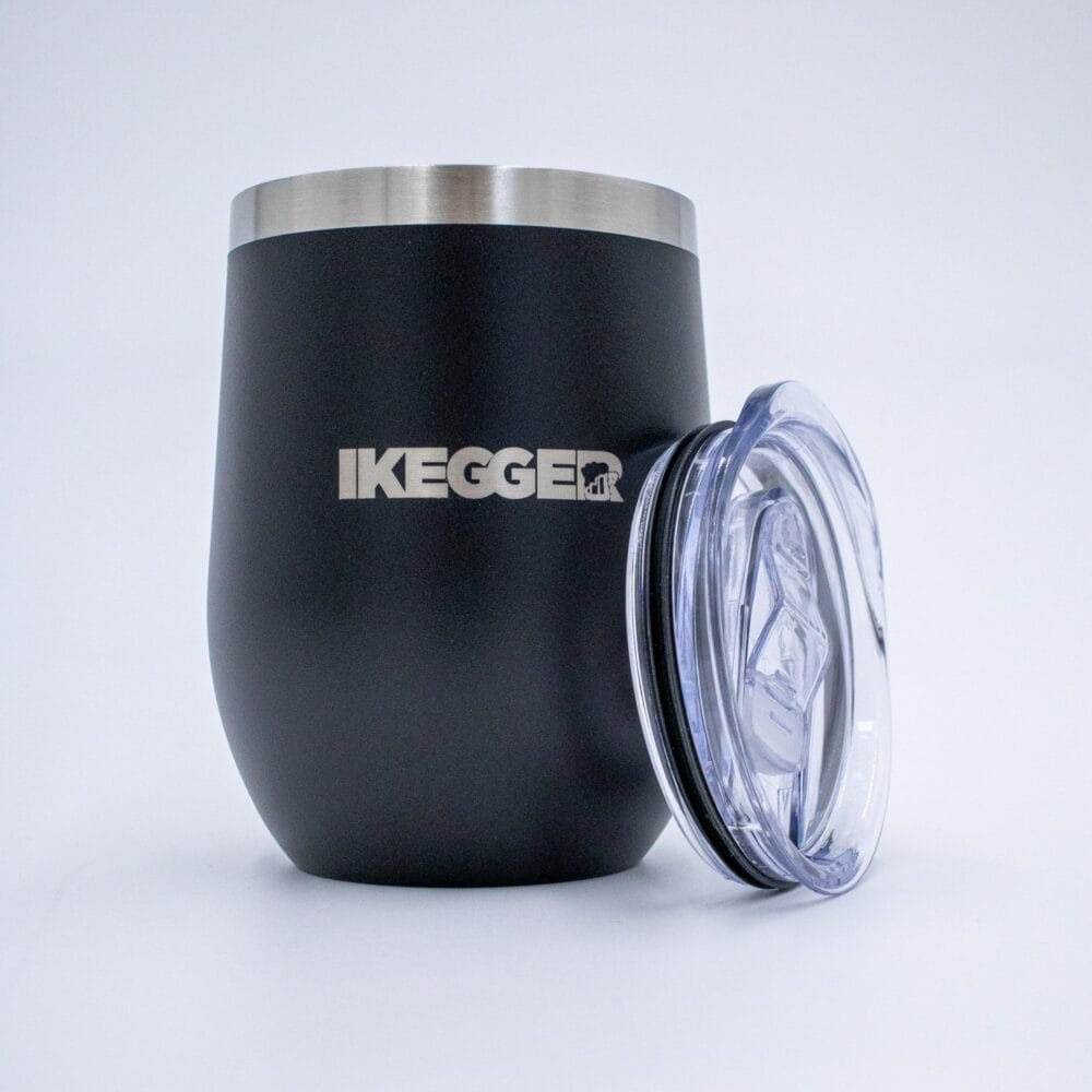 IKG-12OZ Close-up of a matte black cylindrical container with a brushed metal rim at the top and a clear plastic lid on the right; the word 'KEGGER' is partly visible on the side.